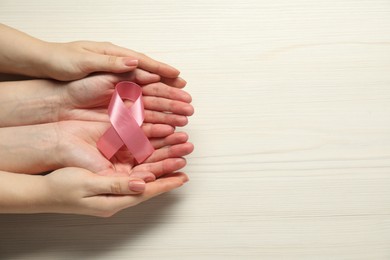 Breast cancer awareness. Women holding pink ribbon at white wooden table, top view. Space for text