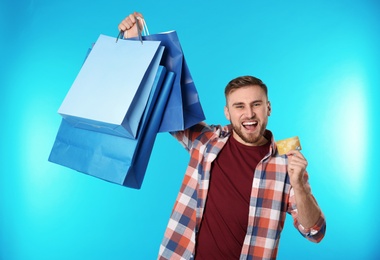 Photo of Portrait of emotional young man with credit card and shopping bags on color background. Spending money