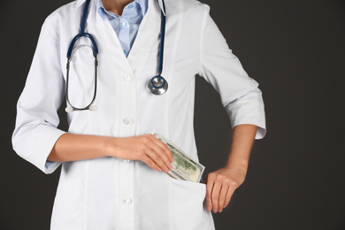 Photo of Doctor putting bribe into pocket on black background, closeup. Corruption in medicine