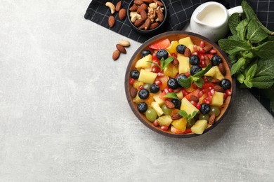 Photo of Delicious fruit salad in bowl, nuts and fresh mint on grey table, flat lay. Space for text