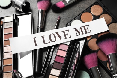 Paper with phrase I Love Me and different makeup products on table, above view