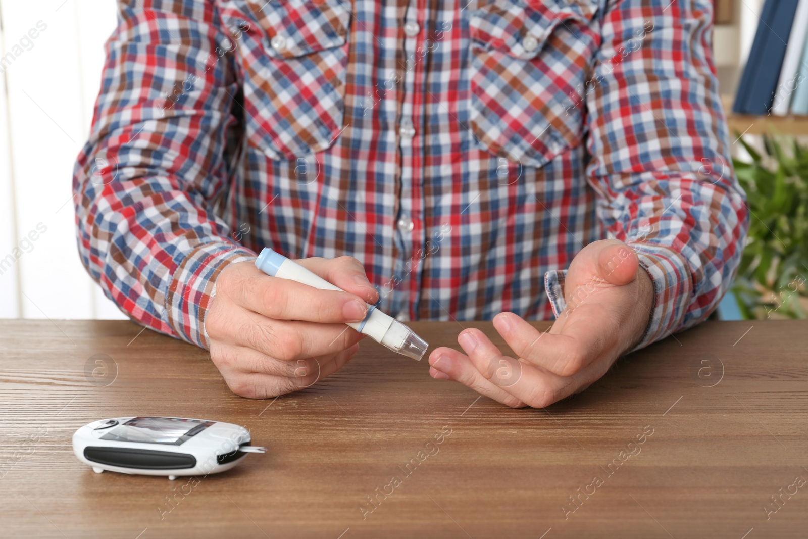Photo of Man using lancet pen at table. Diabetes test