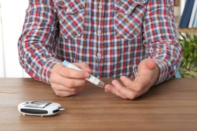 Man using lancet pen at table. Diabetes test