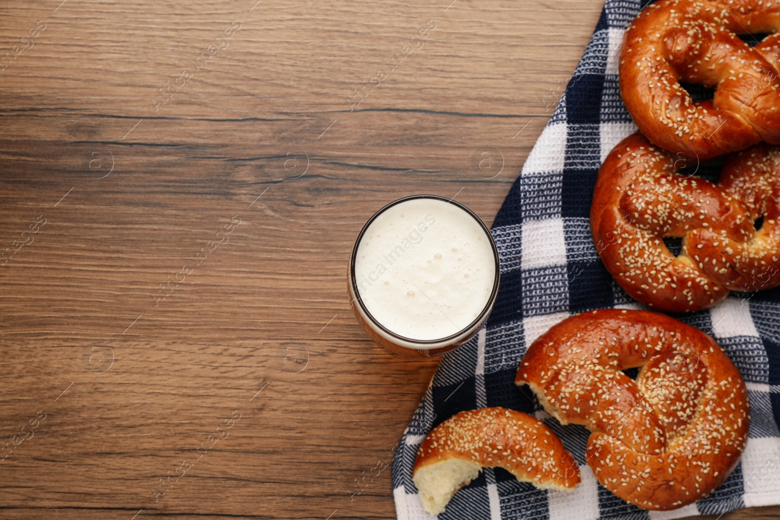 Photo of Tasty pretzels and glass of beer on wooden table, flat lay. Space for text