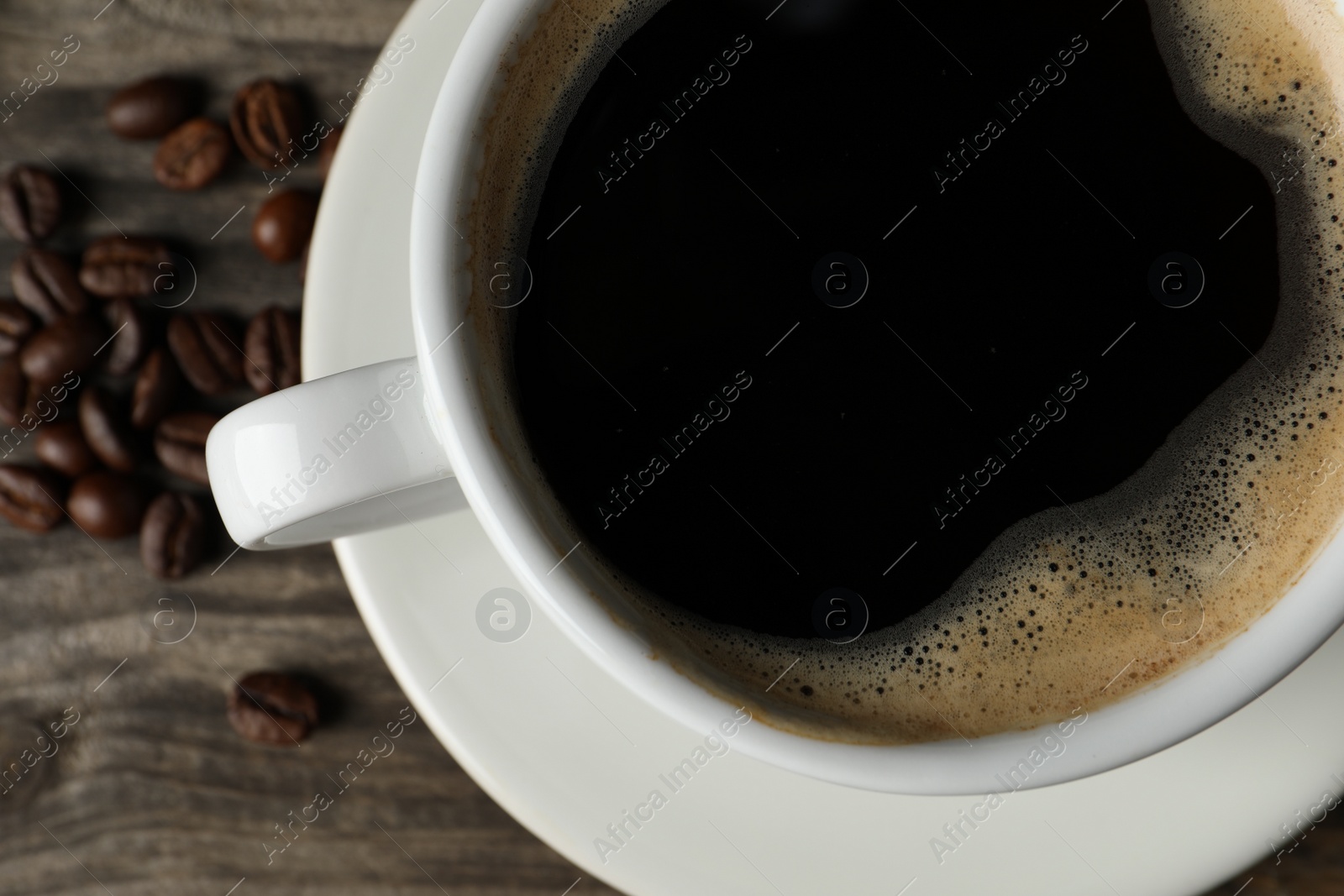 Photo of Cup of hot aromatic coffee and roasted beans on wooden table, flat lay