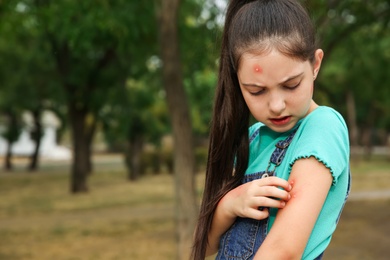 Photo of Girl scratching arm with insect bites in park. Space for text