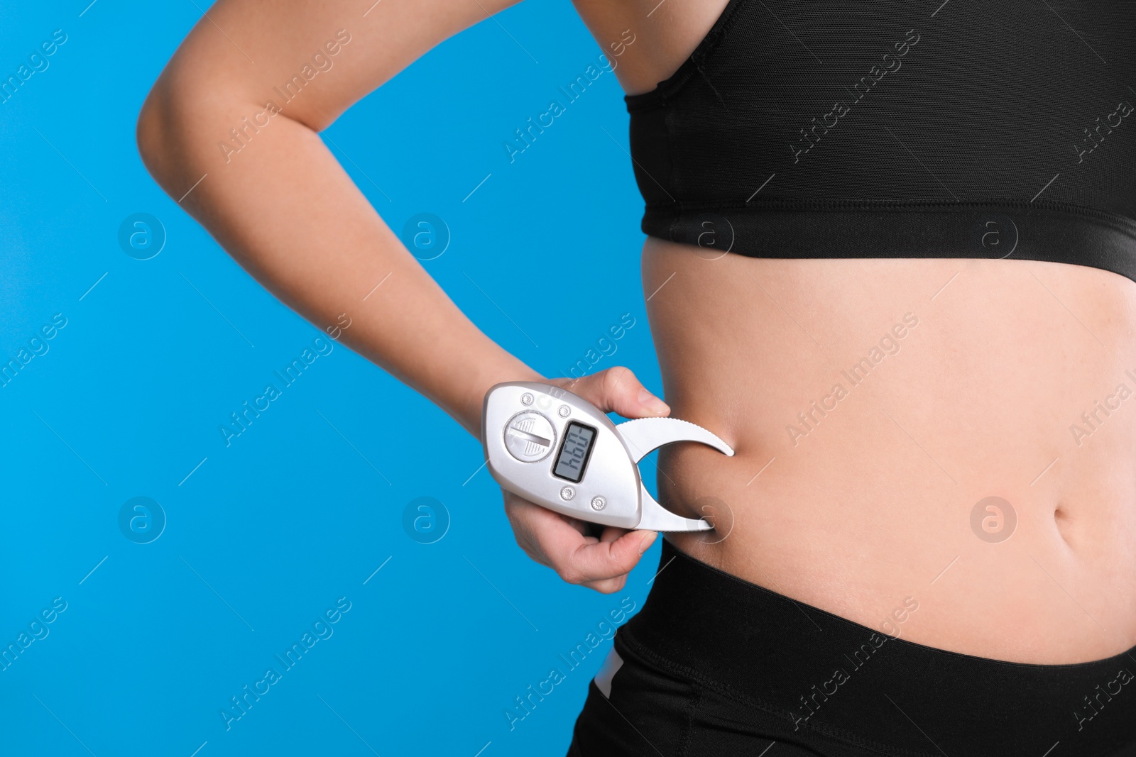 Photo of Young woman measuring body fat with caliper on blue background, closeup. Nutritionist's tool