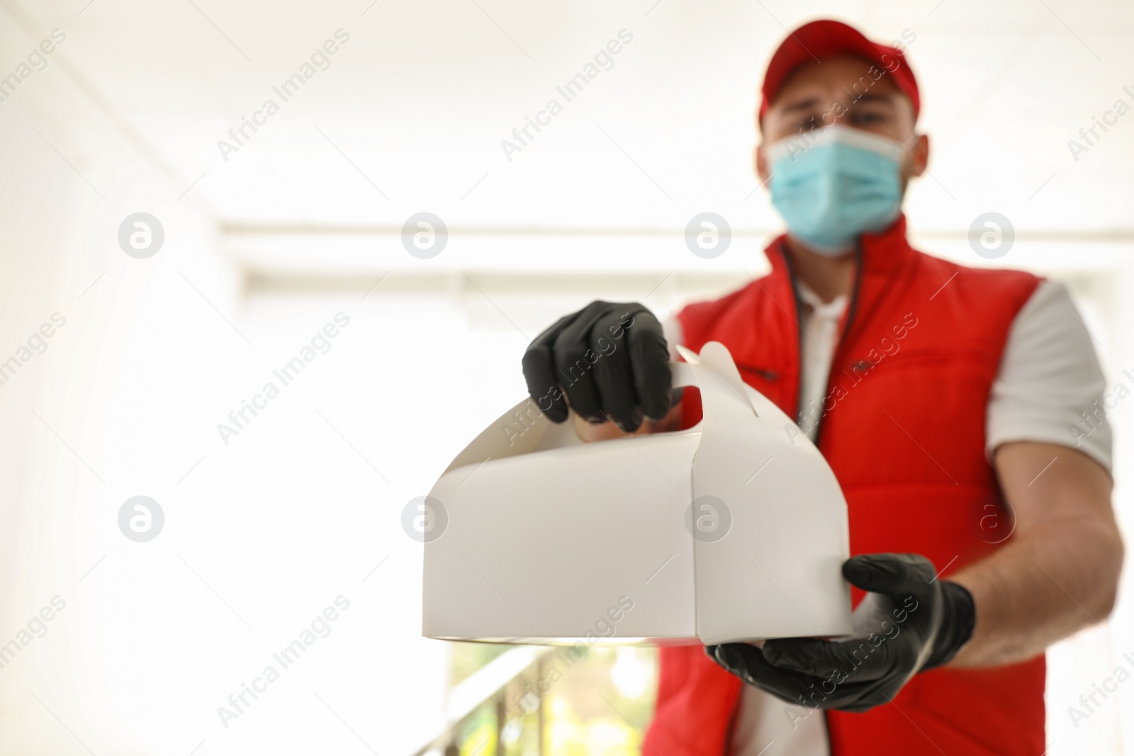 Photo of Courier in protective mask and gloves with order indoors, focus on hands. Restaurant delivery service during coronavirus quarantine