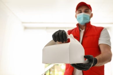 Courier in protective mask and gloves with order indoors, focus on hands. Restaurant delivery service during coronavirus quarantine