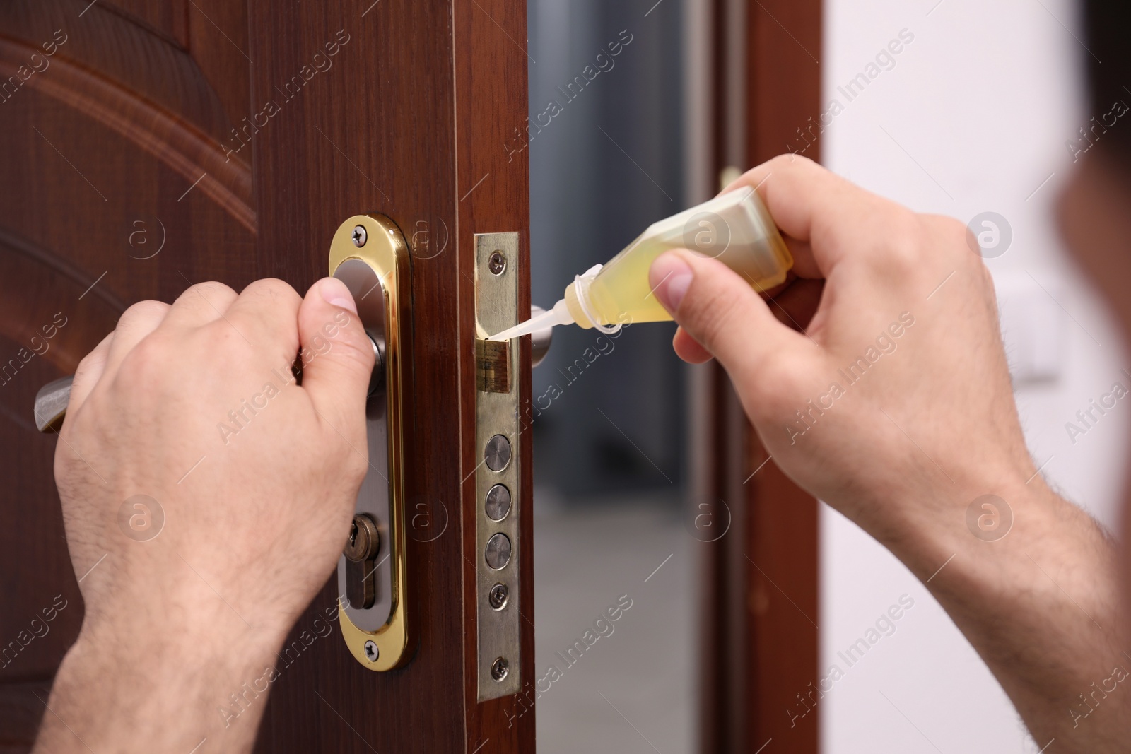 Photo of Repairman lubricating door lock indoors, closeup view
