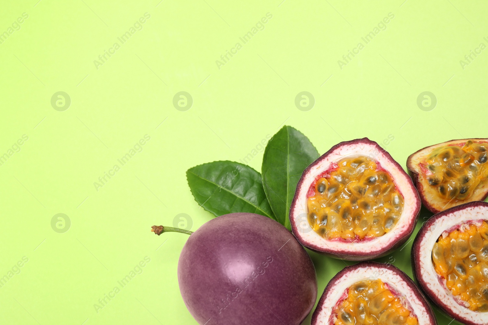 Photo of Fresh ripe passion fruits (maracuyas) with leaves on light green background, flat lay, Space for text