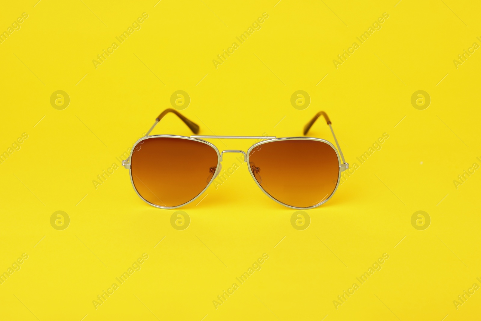 Photo of Stylish pair of sunglasses on yellow background