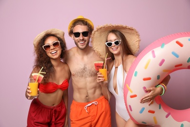 Photo of Happy friends in beachwear with cocktails and inflatable ring on color background