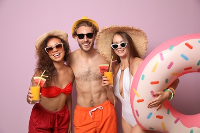 Happy friends in beachwear with cocktails and inflatable ring on color background