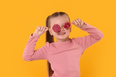 Photo of Happy little girl with bright lollipops covering eyes on orange background