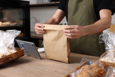 Photo of Seller with paper bag at cashier desk in bakery shop, closeup