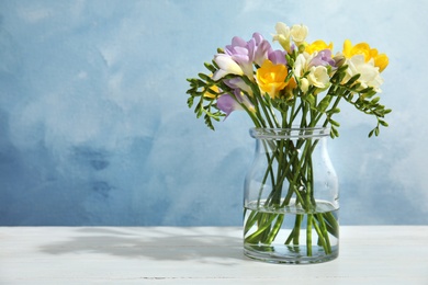 Bouquet of fresh freesia flowers in vase on table. Space for text