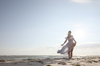 Woman in dress with straw hat walking by sea on sunny day