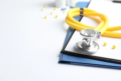 Stethoscope, clipboard and pills on light background, closeup. Medical equipment