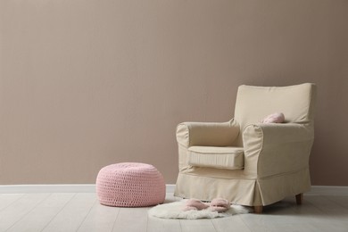 Photo of Knitted pouf, fuzzy rug with slippers and armchair near beige wall indoors. Space for text