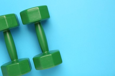 Green dumbbells on light blue background, flat lay. Space for text