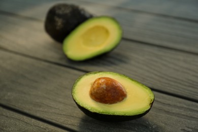 Half and whole fresh avocados on wooden table, closeup