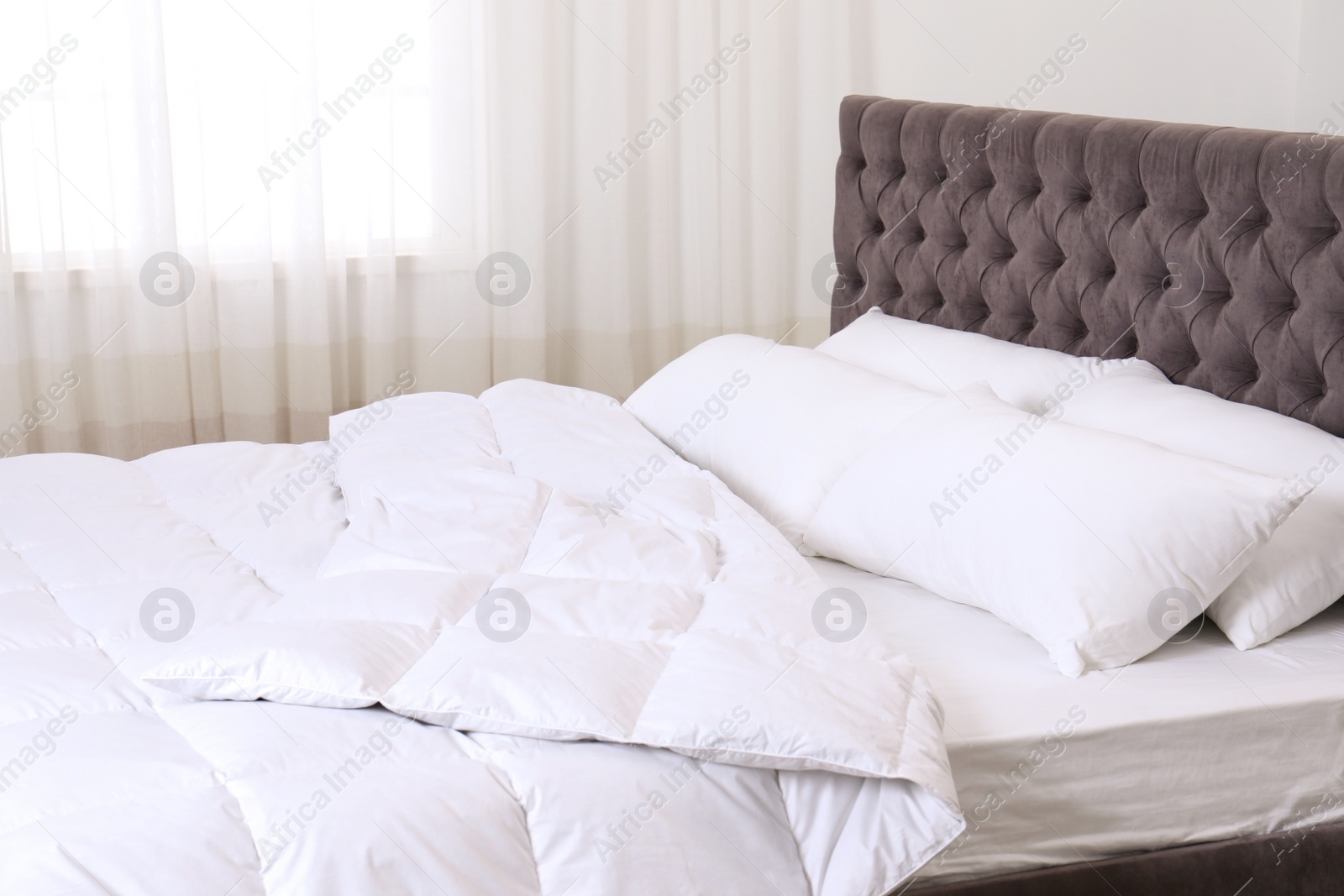 Photo of Large comfortable bed with pillows and blanket near window indoors. Stylish interior