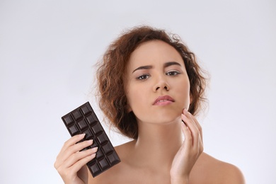 Photo of Beautiful young woman with acne problem holding chocolate on light background. Skin allergy