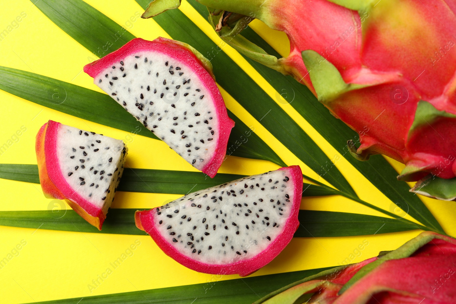 Photo of Slices of delicious white pitahaya fruit with palm leaf on yellow background, flat lay