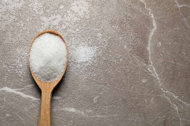 Spoon of white sugar on marble table, top view. Space for text