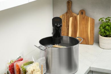 Pot with sous vide cooker and vacuum packed food products in kitchen. Thermal immersion circulator