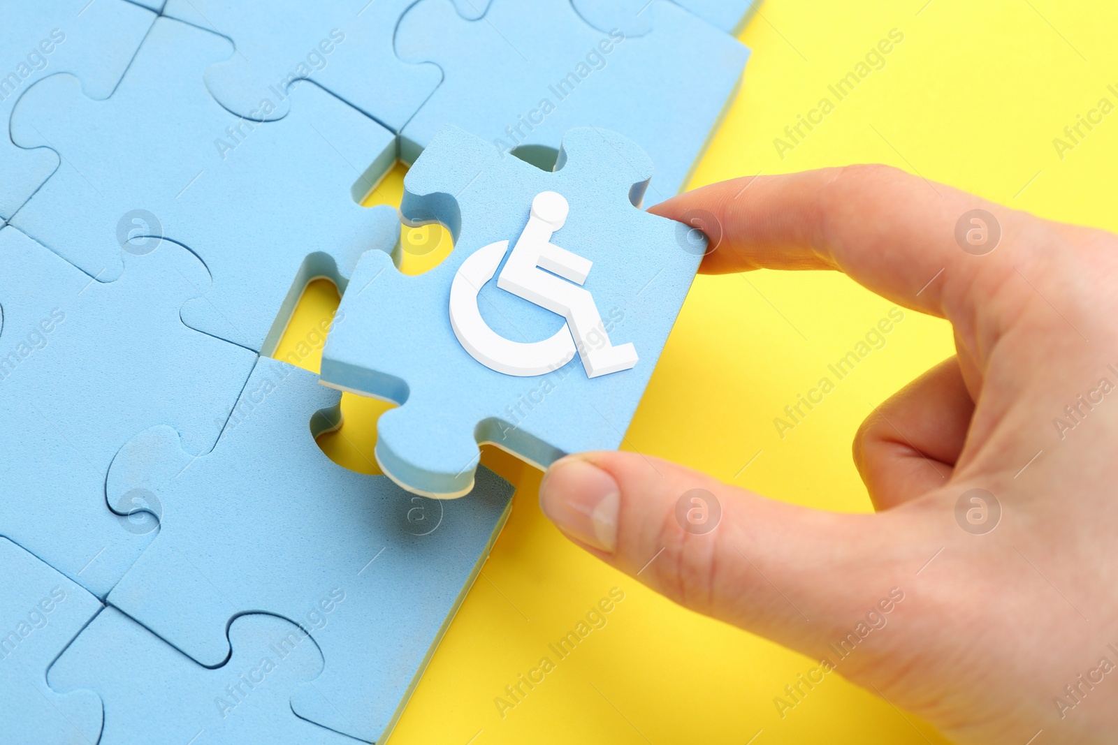 Image of Inclusion concept. Woman putting light blue puzzle with international symbol of access together, closeup