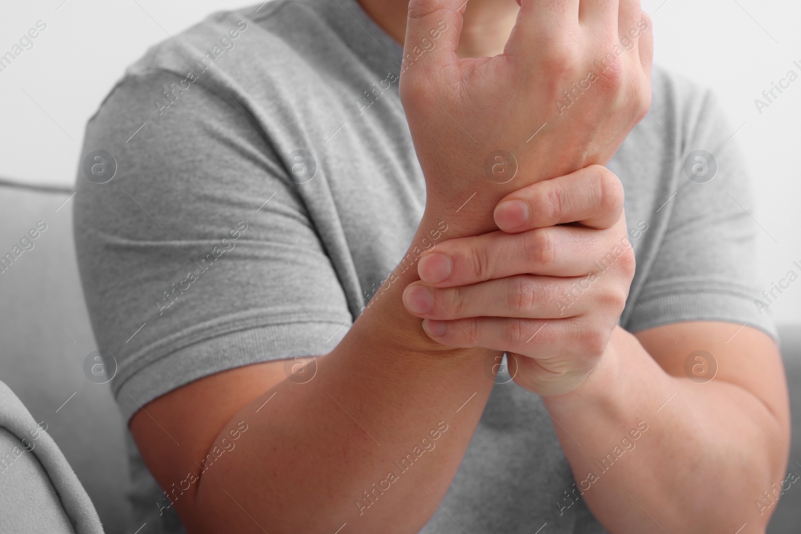 Photo of Man suffering from pain in his hand on armchair indoors, closeup