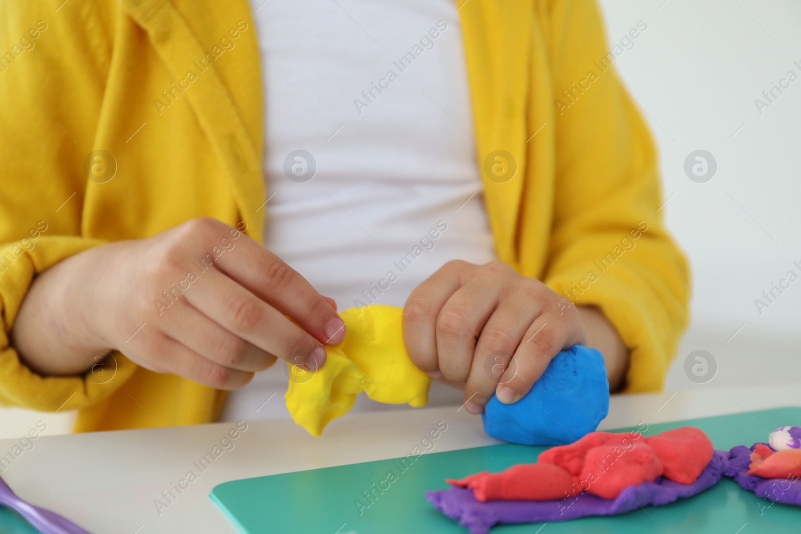 Photo of Little girl sculpting with play dough at white table indoors, closeup