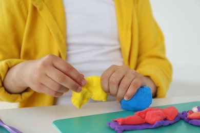 Little girl sculpting with play dough at white table indoors, closeup