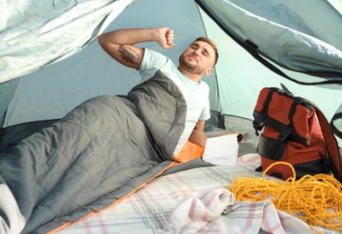 Photo of Young man stretching in sleeping bag inside of camping tent