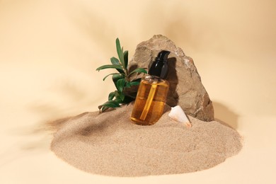 Photo of Bottle of serum, stone and green leaves on sand against beige background