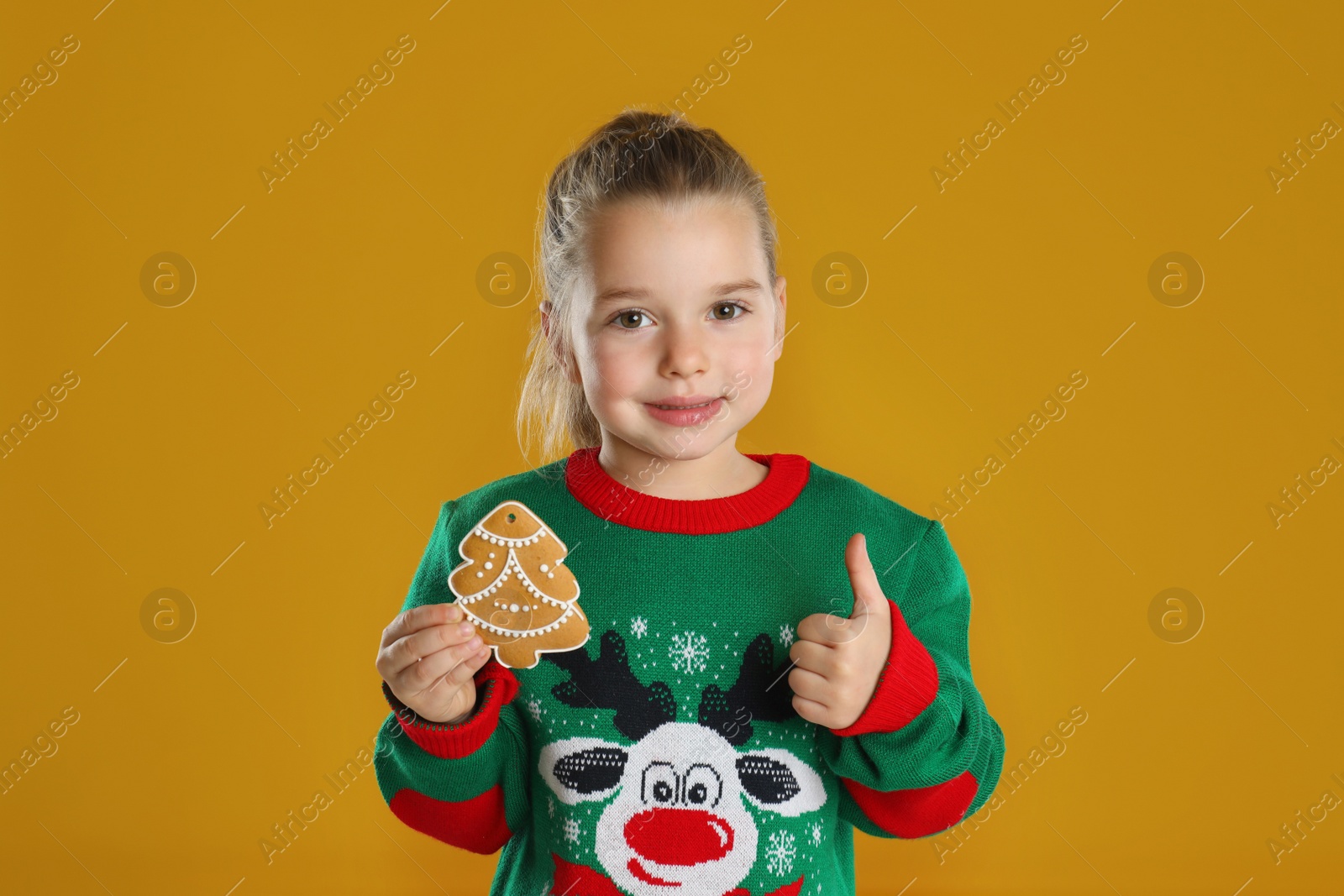 Photo of Cute little girl with Christmas gingerbread cookie on orange background