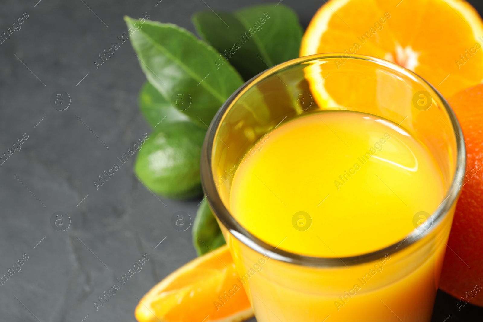 Photo of Glass of orange juice and fresh fruits on dark grey table, closeup