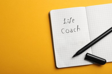 Image of Phrase Life Coach written in notebook and marker on yellow background, top view. Space for text