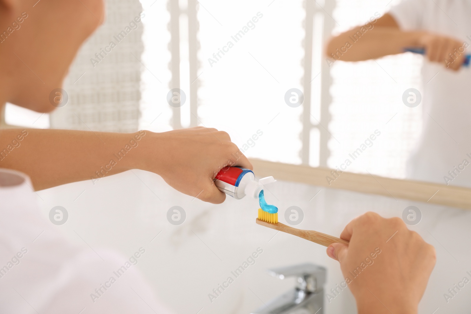 Photo of Woman applying toothpaste on brush in bathroom, closeup