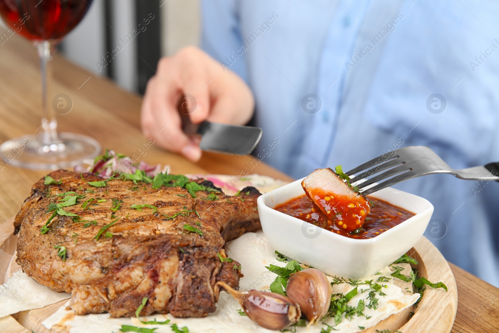 Photo of Woman eating delicious grilled pork chop at wooden table, closeup