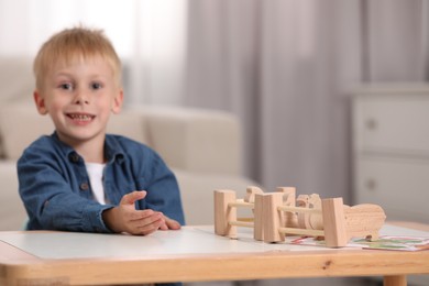 Photo of Cute little boy playing with set of wooden animals and fence at table indoors, selective focus with space for text. Child's toy