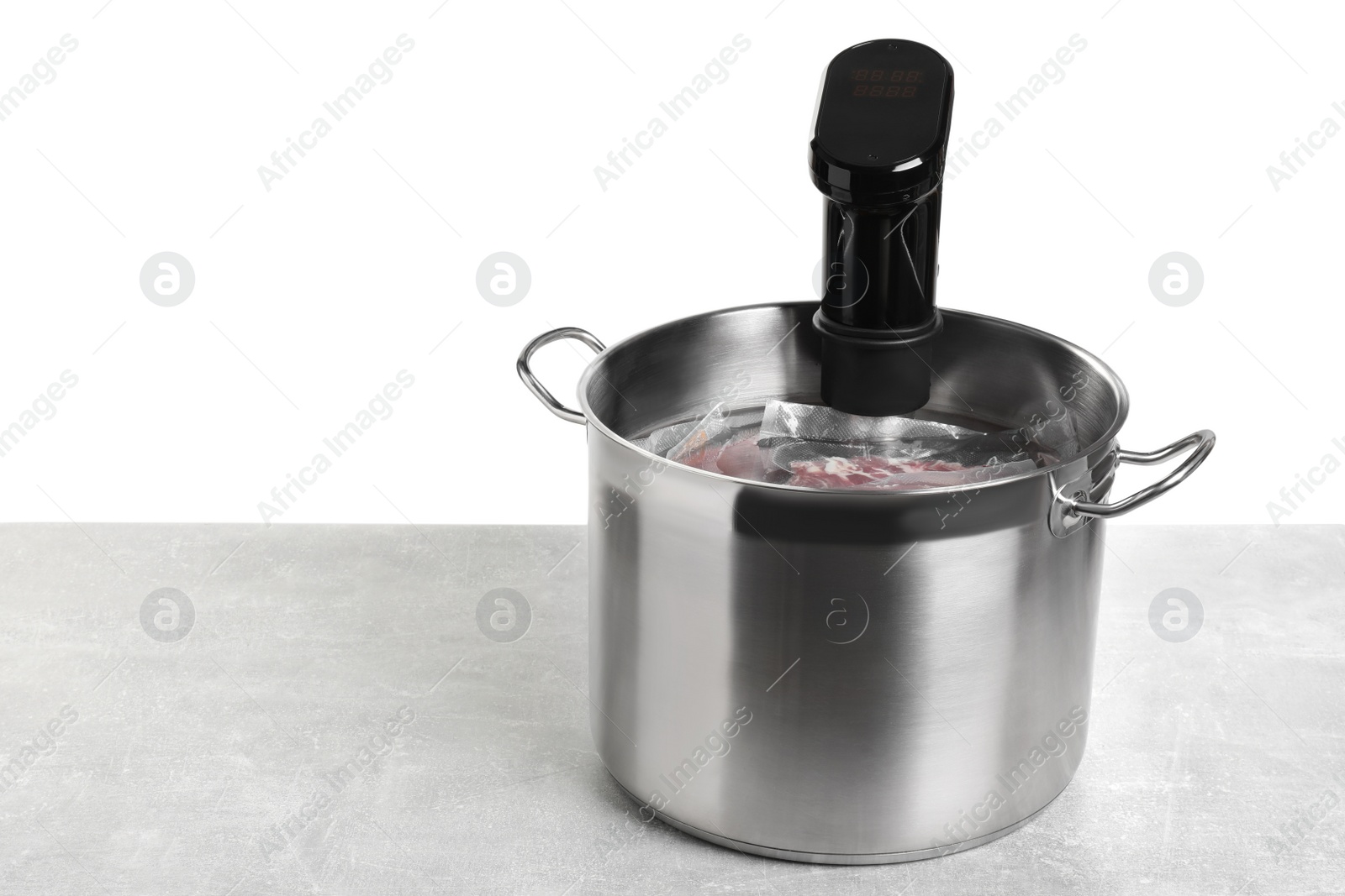 Photo of Sous vide cooker and vacuum packed food products in pot on light marble table against white background, space for text. Thermal immersion circulator