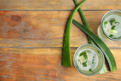 Photo of Fresh aloe drink in glasses and leaves on wooden table, flat lay. Space for text