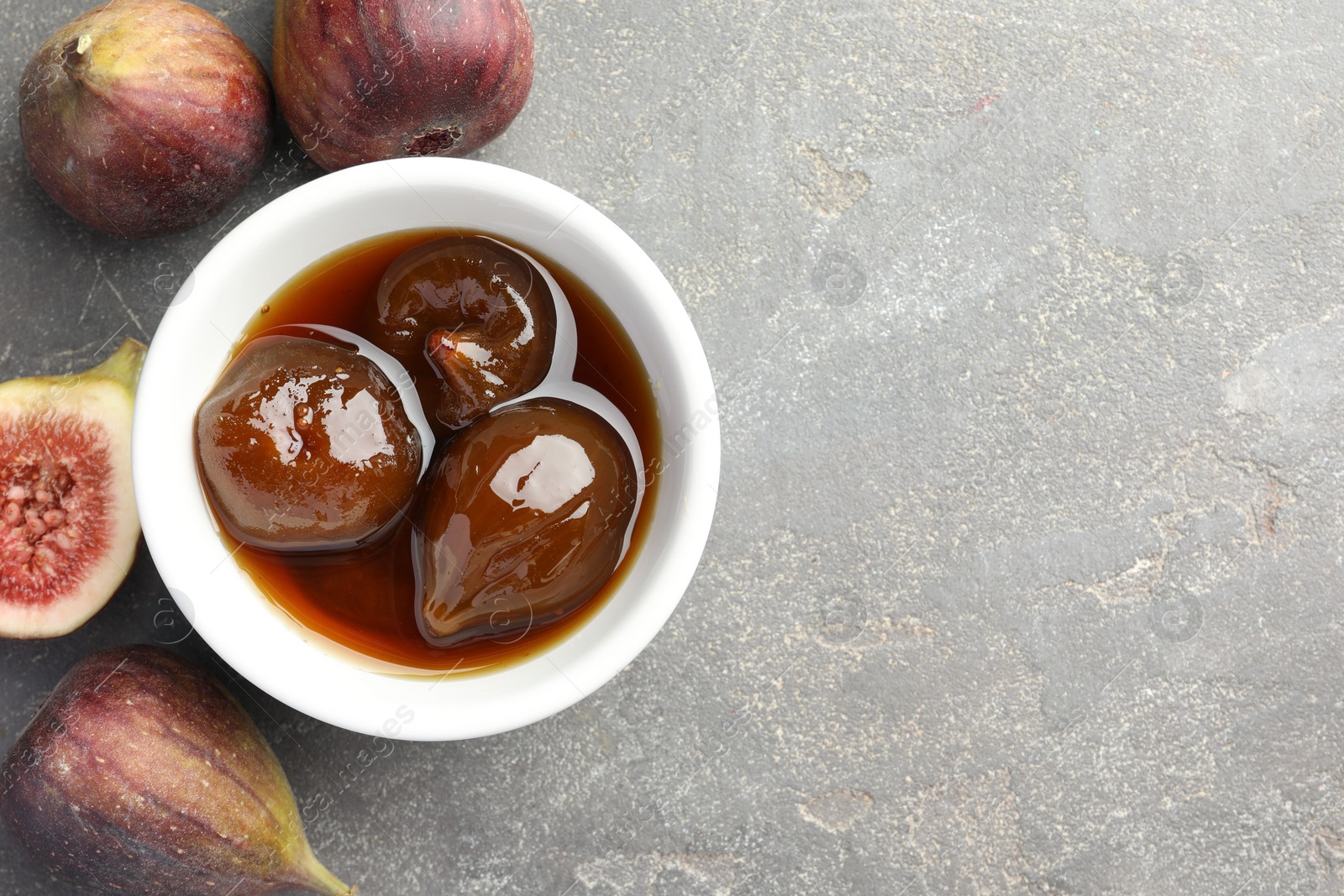 Photo of Bowl of tasty sweet jam and fresh figs on grey table, flat lay. Space for text