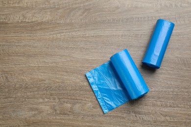 Rolls of light blue garbage bags on wooden table, flat lay. Space for text