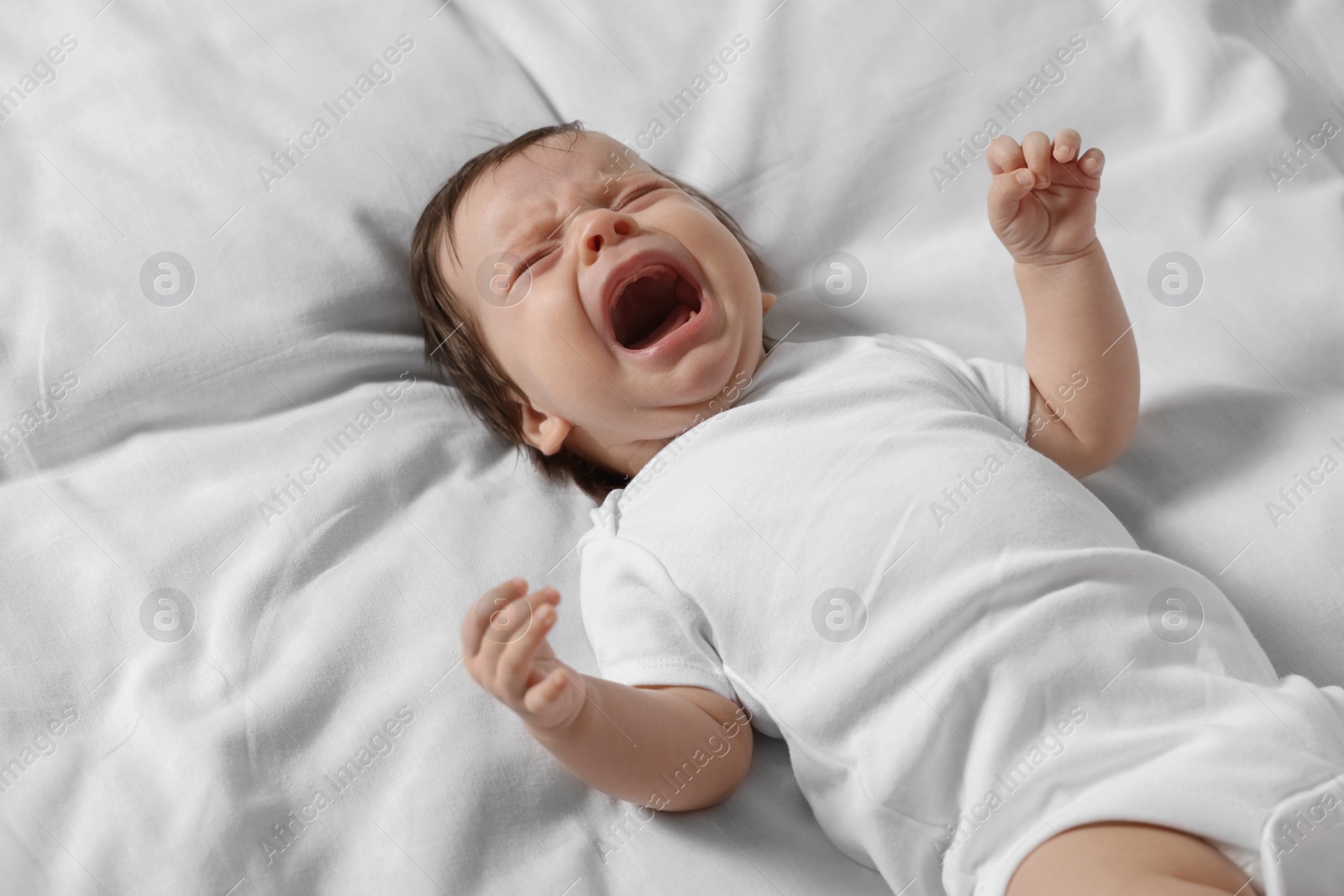 Photo of Crying little baby lying on soft bed