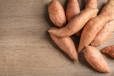 Photo of Pile of sweet potatoes and space for text on wooden background, top view