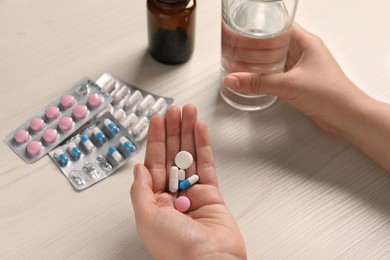 Woman with different pills and glass of water at white wooden table, closeup